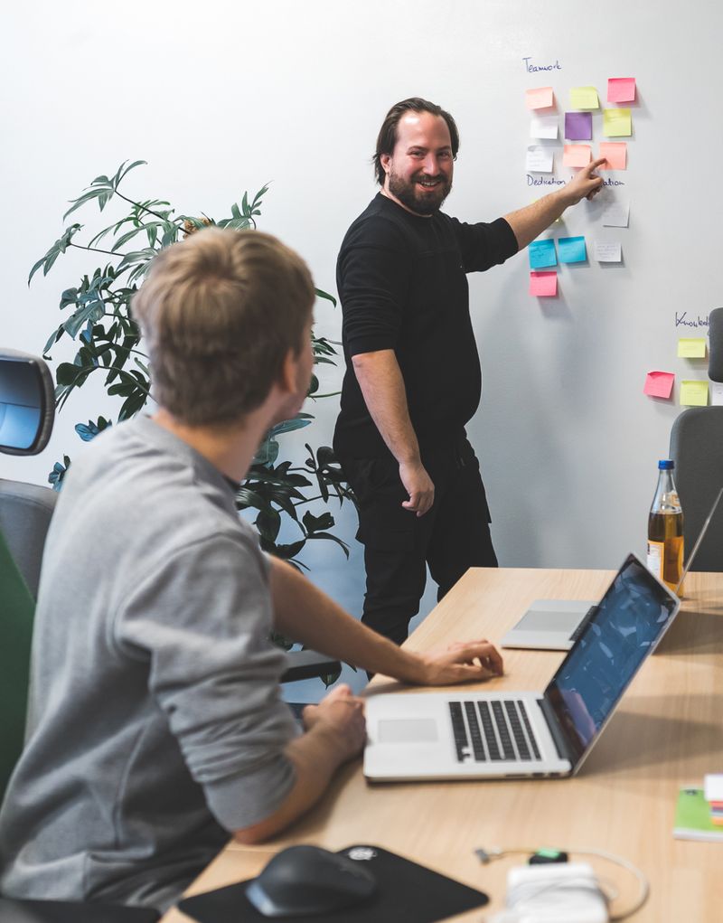 Two people during a meeting at Apptension office, one standing by the wall, pointing to colorful cards there, another looking at the first one